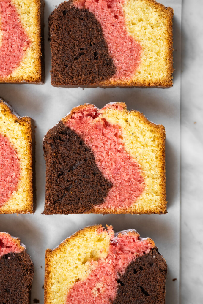 Fatia de bolo napolitano tricolor, com massa marrom de chocolate, rosa de morango e amarela de baunilha. Massa fofa e amanteigada.