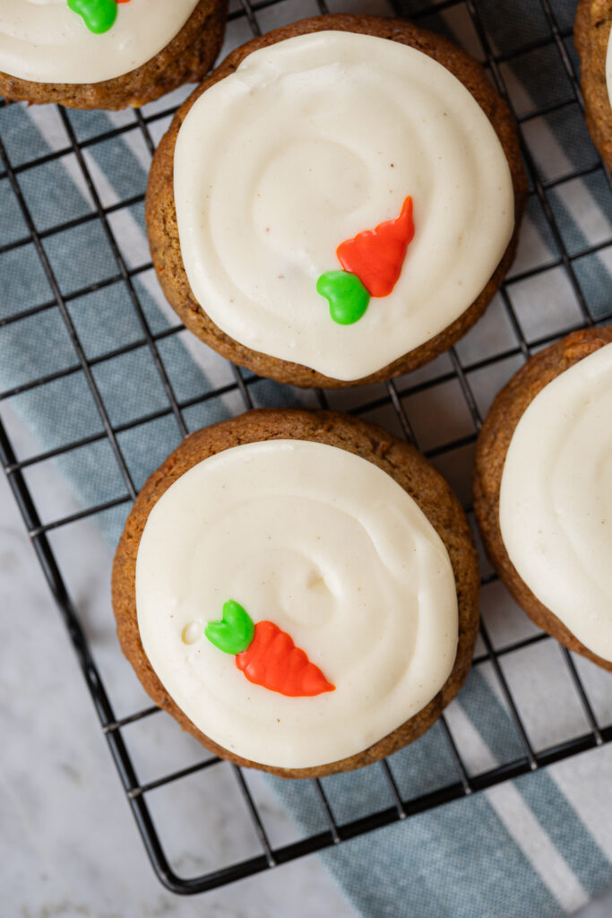 carrot cake cookies decorados com cobertura de cream cheese e cenourinha de glacê, dispostos sobre grade de resfriamento
