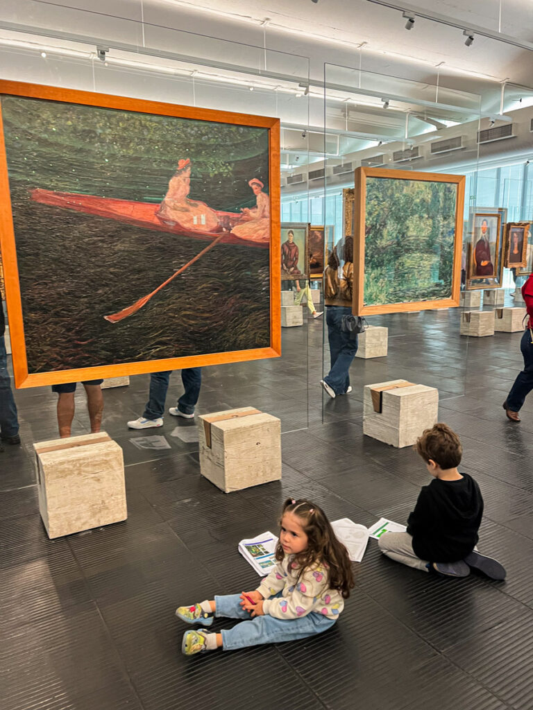 Melissa e Leonardo sentados no chão do MASP com a gincana impressa, em frente a obra de Monet - Visita ao MASP com Crianças
