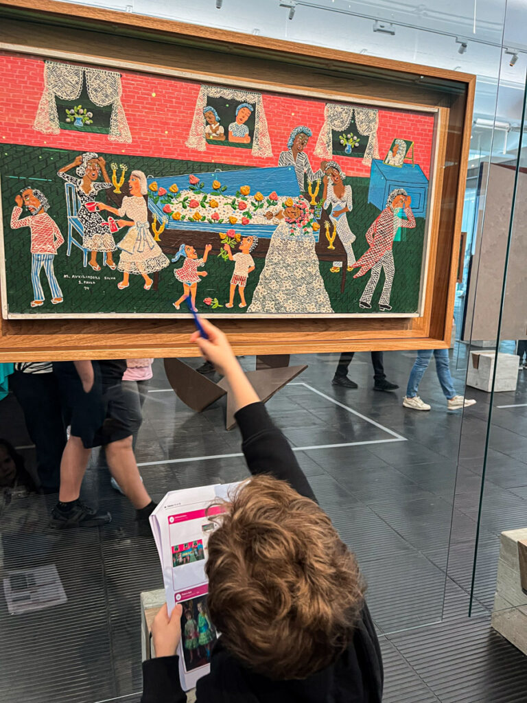Criança apontando detalhes no quadro Velório da Noiva de Maria Auxiliadora no MASP, atividade de arte para crianças - Visita ao MASP com Crianças